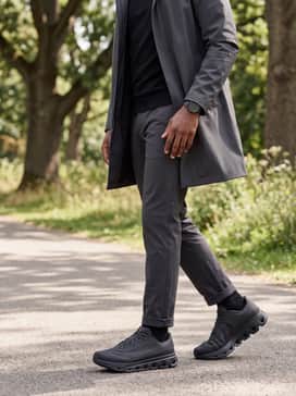 Cloudflow 5 Ad – A sophisticated 'tech-wear' commuter style using tapered charcoal tech-chinos, a black merino wool quarter-zip pullover, and a streamlined waterproof trench coat in a matte finish.