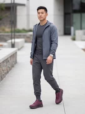 A monochrome gym look featuring charcoal grey moisture-wicking joggers, a matching compression tee, and a light windbreaker in a similar slate tone to let the burgundy shoes pop.