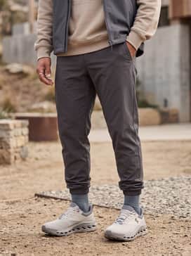 Style with charcoal-toned tapered technical joggers, a sand-colored oversized hoodie, and a lightweight waterproof vest for an urban gorpcore look.