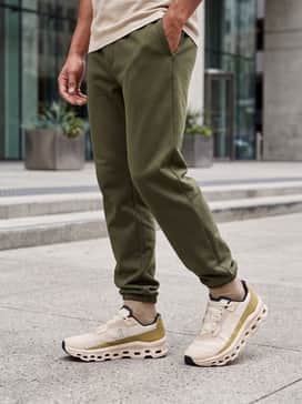 A modern athleisure ensemble consisting of charcoal grey slim-fit joggers, a heavyweight white t-shirt, and an unzipped sage green bomber jacket.