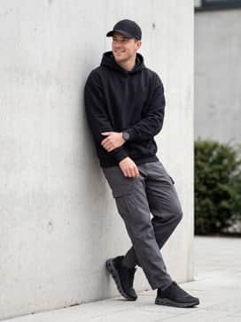 Cloudnova Form 2 Tt – Dark grey cargo pants with an oversized black graphic hoodie and a structured baseball cap for a rugged streetwear-inspired outfit.