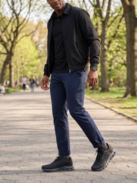 Tailored navy chinos rolled slightly at the ankle with a black polo shirt and a lightweight Harrington jacket for a sharp, sporty-casual vibe.