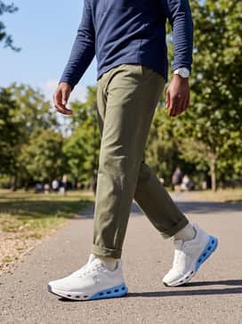 A smart-casual athleisure pairing of slim-fit olive green chinos, a navy blue quarter-zip technical pullover, and a minimalist silver watch to match the shoe's hardware.