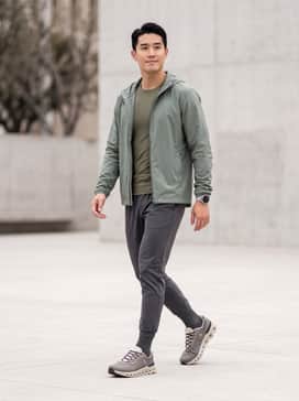 A performance-driven look featuring tapered charcoal grey moisture-wicking joggers, an olive green compression base layer, and a lightweight sage technical windbreaker.