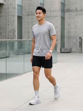 A high-performance running outfit featuring black 5-inch inseam athletic shorts, a moisture-wicking silver-grey technical tee, and low-cut compression socks to highlight the shoe's sleek profile.