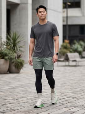 A performance-driven look featuring black compression tights layered under sage green 5-inch running shorts, paired with a fitted, moisture-wicking charcoal grey technical t-shirt.
