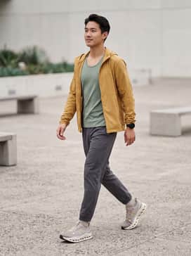 A high-performance running ensemble featuring charcoal grey compression leggings, a moisture-wicking sage green tank top, and a lightweight mustard yellow windbreaker to pick up the shoe's accent colors.