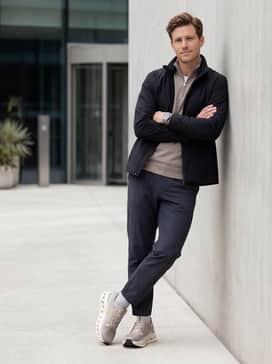 An urban commute outfit with slim-fit navy performance trousers, a breathable light grey merino wool quarter-zip, and a sleek waterproof black shell jacket.