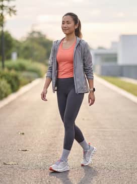High-waisted charcoal compression leggings paired with a moisture-wicking coral racerback tank top and a lightweight grey windbreaker for a cohesive trail-ready look.