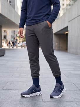 An elevated athleisure ensemble consisting of charcoal grey tapered joggers, a fitted navy blue quarter-zip pullover, and a sleek waterproof shell jacket.