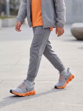 Grey tapered joggers paired with a bright orange moisture-wicking t-shirt and a lightweight grey windbreaker for a coordinated athletic look.