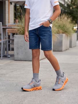 Dark blue denim shorts with a white graphic tee featuring orange accents, topped with a baseball cap for a cool, casual weekend outfit.