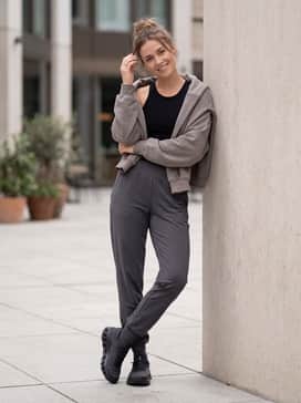 A modern athleisure outfit consisting of black compression leggings or high-performance joggers, a fitted racerback tank, and an oversized cropped hoodie in a neutral stone shade.