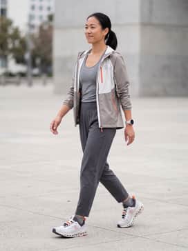 Cloudultra 2 – High-waisted charcoal compression leggings paired with a light grey moisture-wicking racerback tank and a technical windbreaker featuring orange zippers to match the shoe accents.
