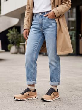 Light-wash boyfriend jeans cuffed at the ankle with a tucked-in white graphic tee and a tan trench coat for an effortless city vibe.