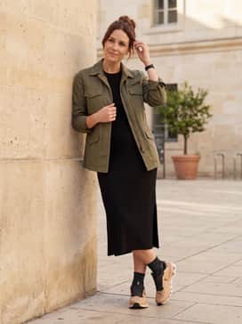 A black midi-length ribbed knit dress layered with an olive green utility jacket for a sporty-chic weekend ensemble.