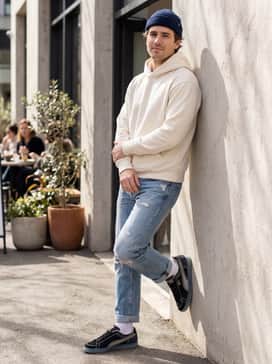Style with distressed light-wash straight-leg jeans, a heavy-weight cream hoodie, and a navy blue beanie for a relaxed, textured ensemble.