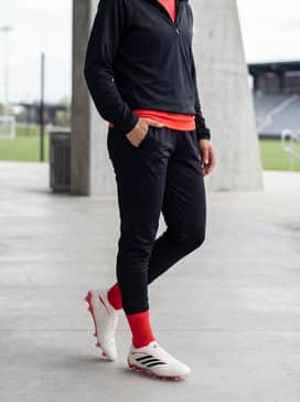 A training-focused ensemble consisting of black tapered soccer joggers, a fitted solar red training top to match the shoe's accents, and a lightweight quarter-zip pullover.