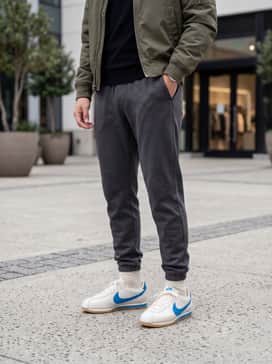 Cortez Leather – Dark grey tapered joggers matched with a black fitted turtleneck sweater and a classic olive green bomber jacket for a modern urban look.
