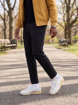 Black tailored joggers worn with a fitted black turtleneck and a mustard yellow bomber jacket to echo the shoe's color pop.