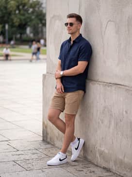 Tan chino shorts worn with a navy linen short-sleeved button-down and polarized sunglasses for a clean, summer-appropriate outfit.