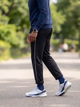 Slim-fit black track pants with white side stripes, a navy blue quarter-zip pullover, and a sleek silver-toned sports watch to complement the shoe's accents.