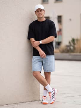 Crazyquick Padel Shoes – A relaxed summer casual ensemble with slim-fit light wash denim shorts, a basic black oversized tee, and a white baseball cap.
