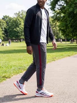 Crazyquick Padel Shoes – A sleek off-duty style pairing charcoal grey track pants with a red side stripe, a white graphic t-shirt, and a lightweight black bomber jacket.