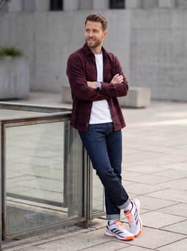 A casual off-court ensemble pairing slim-fit indigo jeans with a simple white crewneck tee and a dark red flannel shirt worn open to tie in the shoe's side-wall detailing.
