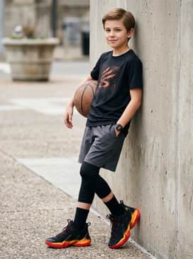 Black athletic compression leggings worn under loose charcoal training shorts with a vibrant orange graphic tee to highlight the shoe's gradient.