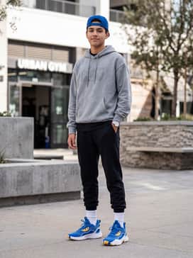 Urban streetwear featuring black tapered cargo joggers, an oversized grey graphic hoodie, and a blue snapback cap that echoes the shoe color.