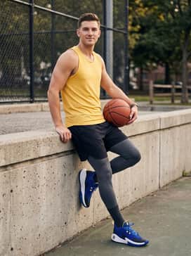 A gym-ready outfit with charcoal compression leggings worn under black athletic shorts, paired with a fitted yellow performance tank top to echo the shoe's accents.