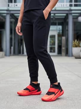 Sleek black tapered tech-fleece joggers paired with a compression long-sleeve top and a lightweight charcoal grey zip-up hoodie for pre-game warm-ups.