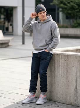 Dark-wash stacked denim jeans with a grey oversized hoodie and a beanie that features subtle orange embroidery.