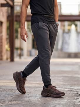 An urban training look with black tapered tech joggers, a fitted olive green compression long-sleeve tee, and a lightweight technical running vest.