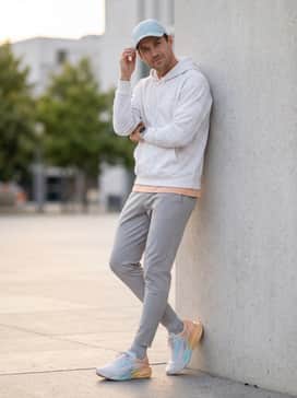 A post-run transition look with tapered light grey joggers, an oversized white graphic hoodie, and a matching pastel-toned baseball cap.