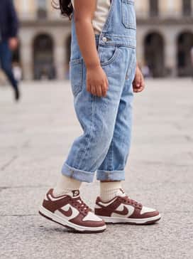 Classic light-wash denim overalls worn over a crisp white long-sleeve tee, creating a timeless, durable, and play-ready outfit that lets the shoes pop.