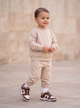 A soft beige cotton tracksuit with subtle gold accents to complement the warm palette and the sophisticated embossed leather details of the sneaker.