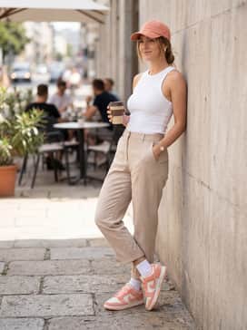 Relaxed-fit beige cargo pants and a fitted white ribbed tank top, accessorized with a matching peach baseball cap for a modern streetwear aesthetic.