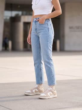 High-waisted light wash straight-leg denim jeans paired with a cropped white baby tee and a delicate gold layered necklace set to match the shoe's metallic accents.