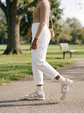White cargo pants styled with a fitted tan turtleneck and a coordinating earth-toned crossbody bag for a functional streetwear aesthetic.