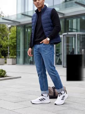 A clean weekend outfit consisting of slim-fit dark blue jeans, a basic black crewneck sweater, and a navy quilted vest.