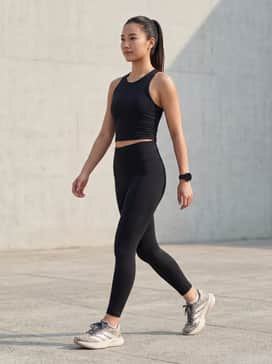 Black high-waisted compression leggings paired with a matching black moisture-wicking cropped tank top and a sleek ponytail for a focused gym session.