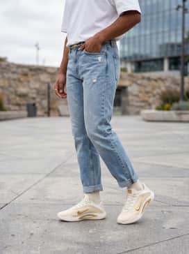 High-waisted light wash distressed denim jeans with a tucked-in oversized white heavy-cotton tee and a thin gold chain belt.