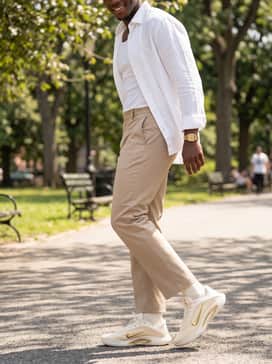 Dynasty – Tailored beige chinos paired with a crisp white linen shirt left unbuttoned over a ribbed tank top for a sophisticated summer streetwear look.