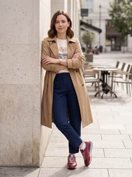 Relaxed navy blue trousers with a tucked-in graphic tee and a tan trench coat for a sophisticated yet sporty city look.