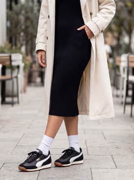 Easy Rider Vintage Womens Sneakers – A black ribbed midi sweater dress paired with an oversized cream trench coat to balance sporty comfort with sophisticated lines.