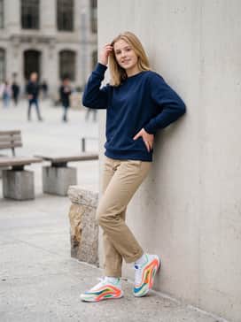 Everlasting – Cuffed khaki chinos worn with a navy blue crewneck sweatshirt and white athletic socks to highlight the primary color palette.