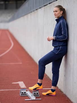 A tapered navy blue track suit with white piping, worn as a warm-up layer before stepping onto the starting blocks.