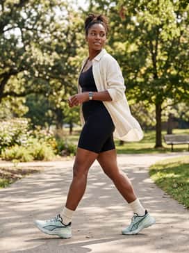 A sleek athleisure style using black biker shorts, a matching scoop-neck sports bra, and an unbuttoned cream-colored linen shirt for an effortless layer.